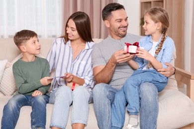 Cute little children presenting their parents with gifts on sofa at home