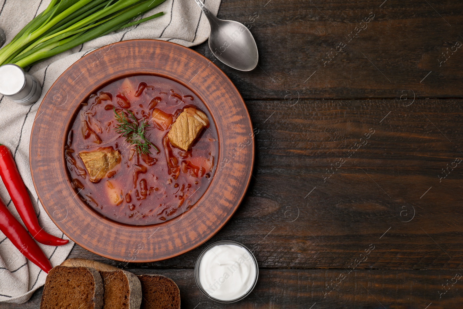 Photo of Bowl of delicious borscht, green onions, sour cream and chili peppers on wooden table, flat lay. Space for text