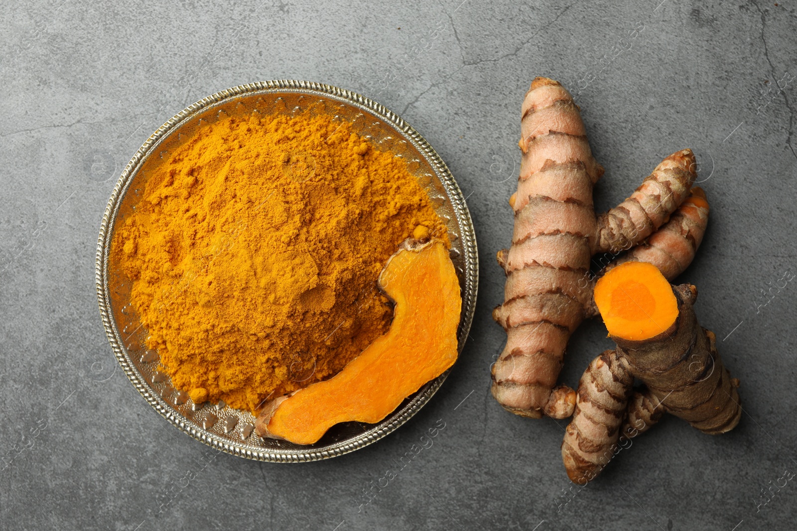 Photo of Plate with turmeric powder and raw roots on grey table, flat lay