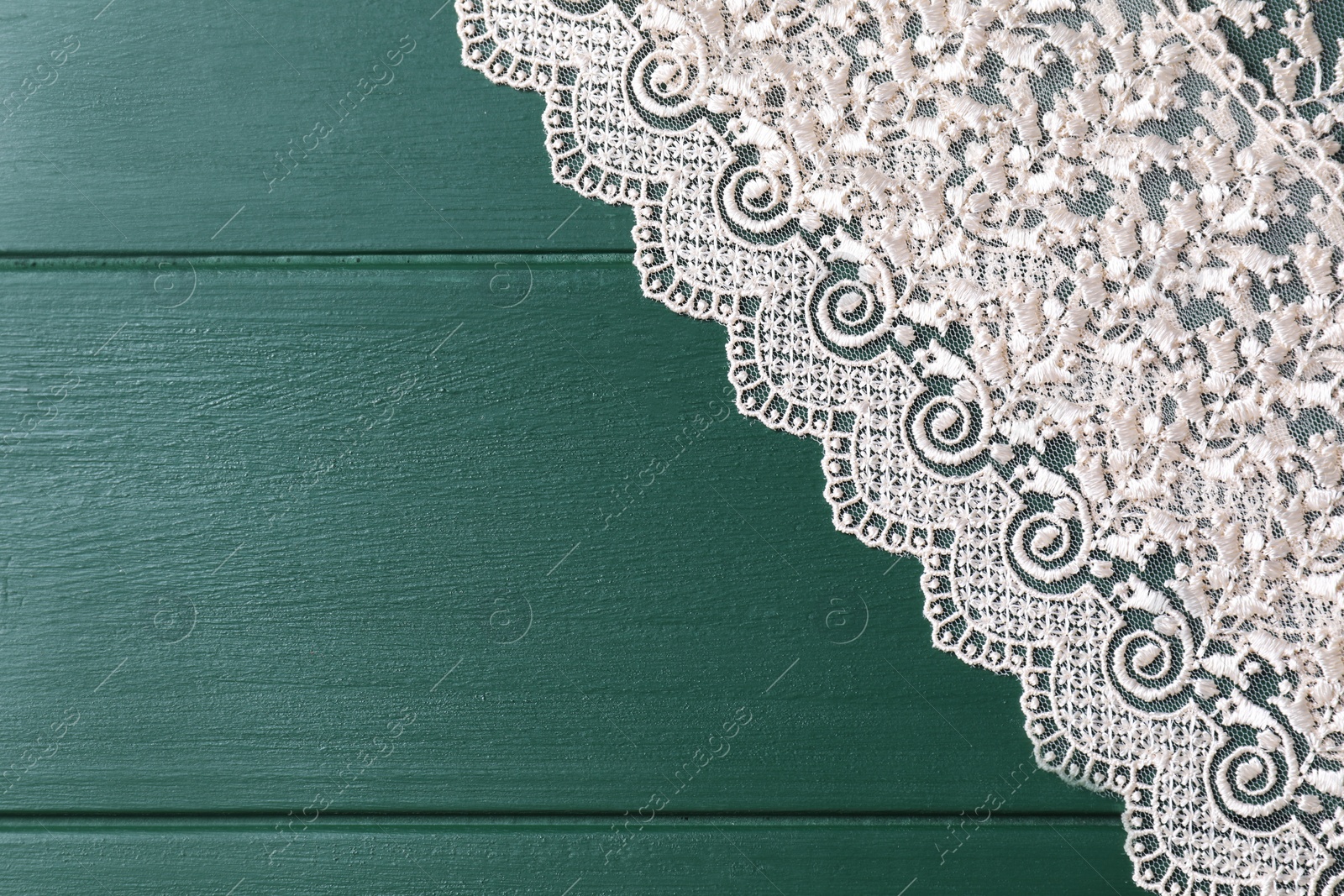 Photo of Beige lace on green wooden table, top view. Space for text