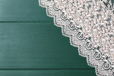 Beige lace on green wooden table, top view. Space for text