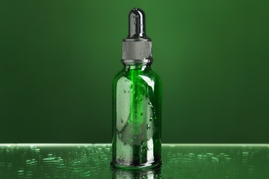 Photo of Bottle of face serum on wet surface against green background, closeup