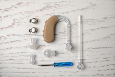 Photo of Flat lay composition with hearing aid and accessories on white wooden background
