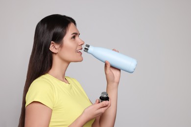 Photo of Young woman drinking from thermo bottle on light grey background. Space for text