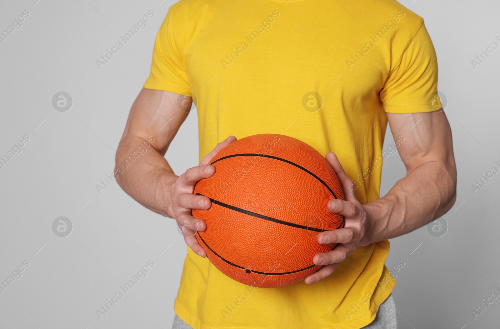 Photo of Athletic young man with basketball ball on light grey background, closeup