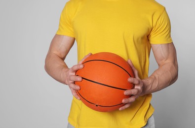 Athletic young man with basketball ball on light grey background, closeup