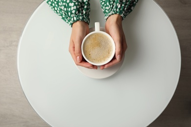 Photo of Woman with cup of coffee at white table indoors, top view