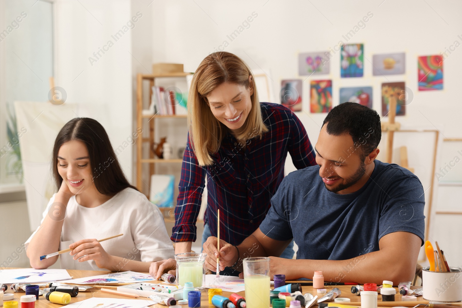 Photo of Artist teaching her students to paint at table in studio. Creative hobby