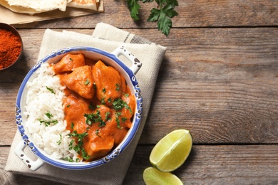 Delicious butter chicken with rice served on wooden table, flat lay. Space for text