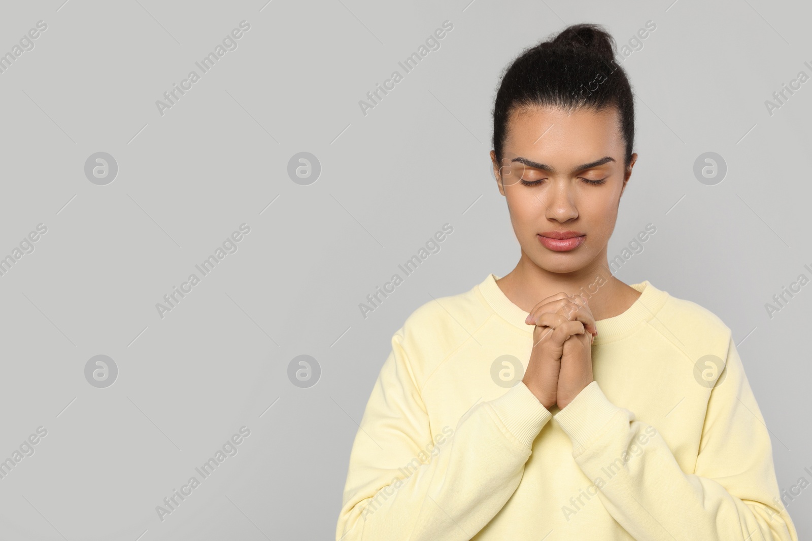 Photo of African American woman with clasped hands praying to God on light grey background. Space for text