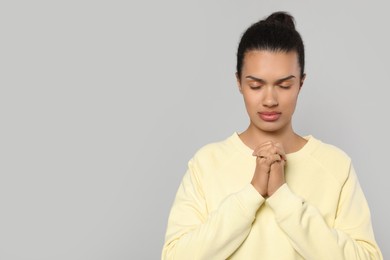 Photo of African American woman with clasped hands praying to God on light grey background. Space for text