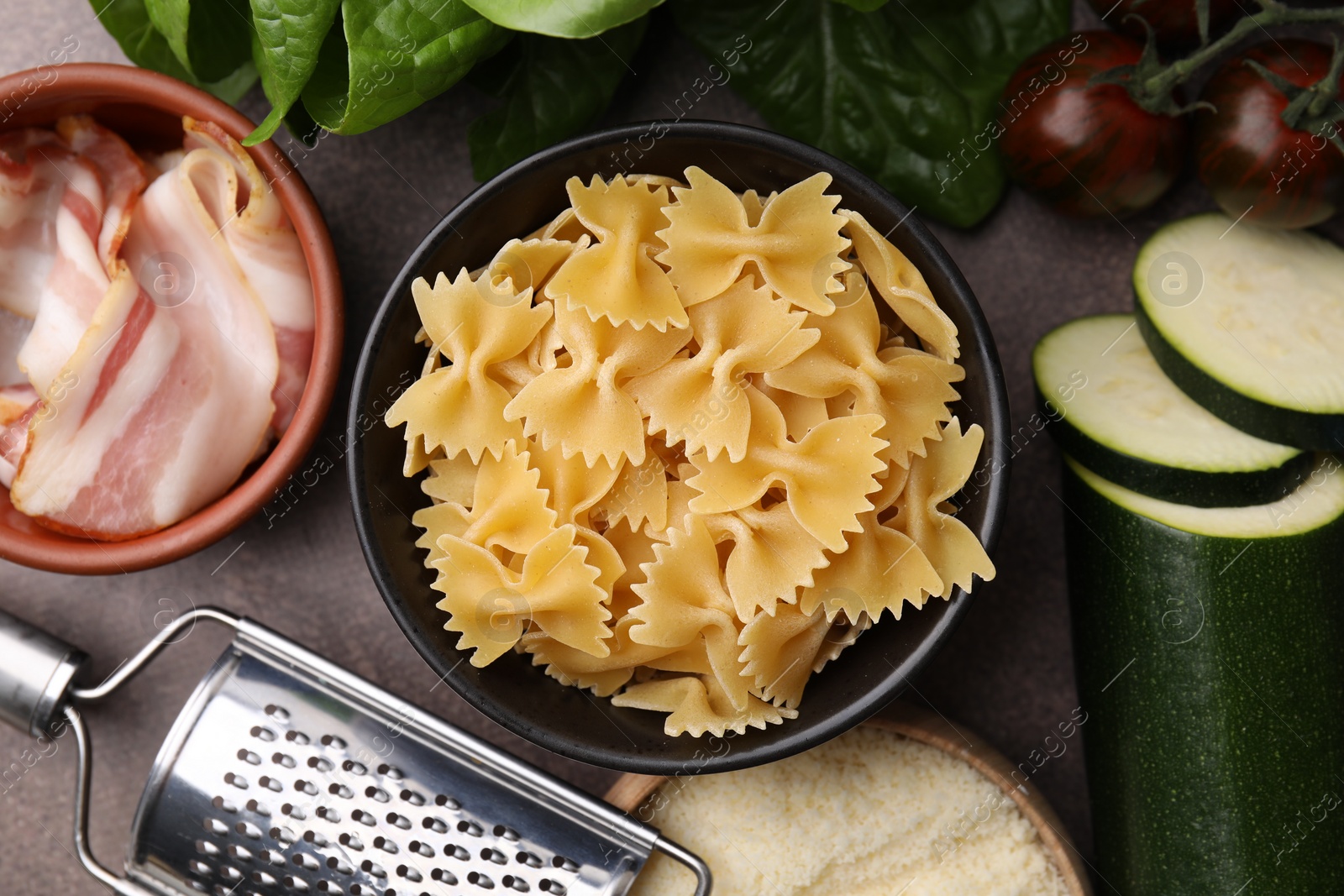 Photo of Raw pasta, bacon and fresh ingredients on brown table, flat lay