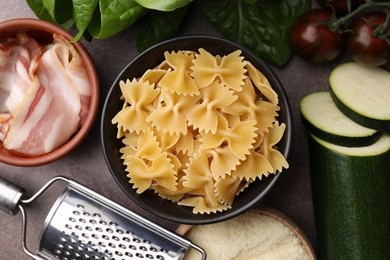 Photo of Raw pasta, bacon and fresh ingredients on brown table, flat lay