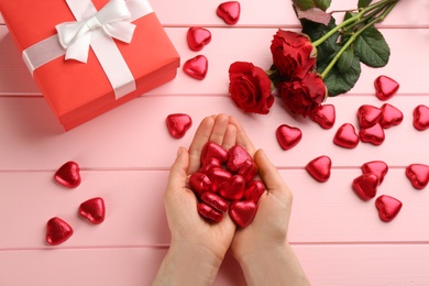 Photo of Woman holding heart shaped chocolate candies at pink wooden table, top view