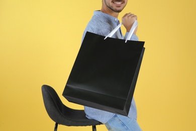 Young man holding paper bag on color background, closeup.  Mockup for design