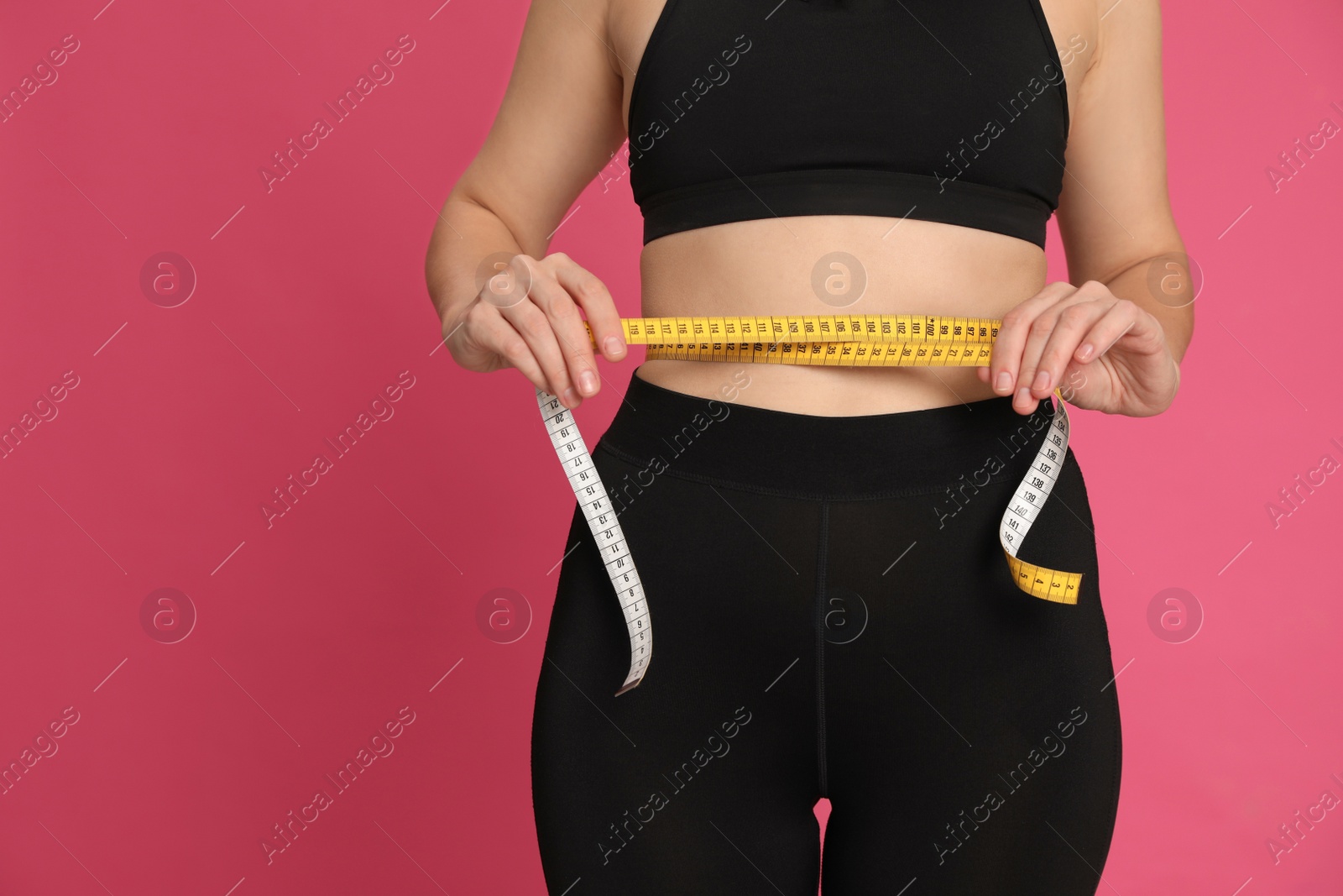 Photo of Woman measuring waist with tape on pink background, closeup. Space for text