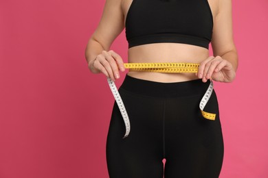 Woman measuring waist with tape on pink background, closeup. Space for text