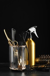 Different hairdresser tools on grey table against black background