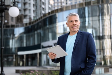 Portrait of handsome mature man with tablet in city center. Space for text