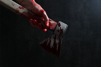 Man holding bloody axe on dark gray background, closeup