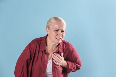 Mature woman having heart attack on color background