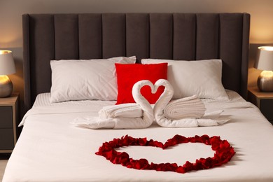 Honeymoon. Swans made with towels and heart of beautiful rose petals on bed in room