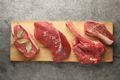 Photo of Pieces of raw beef meat and spices on grey textured table, top view