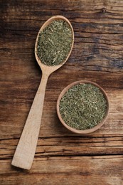 Photo of Bowl and spoon of dried dill on wooden table, flat lay