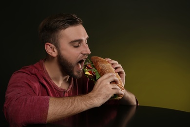 Photo of Young man eating tasty burger on color background. Space for text