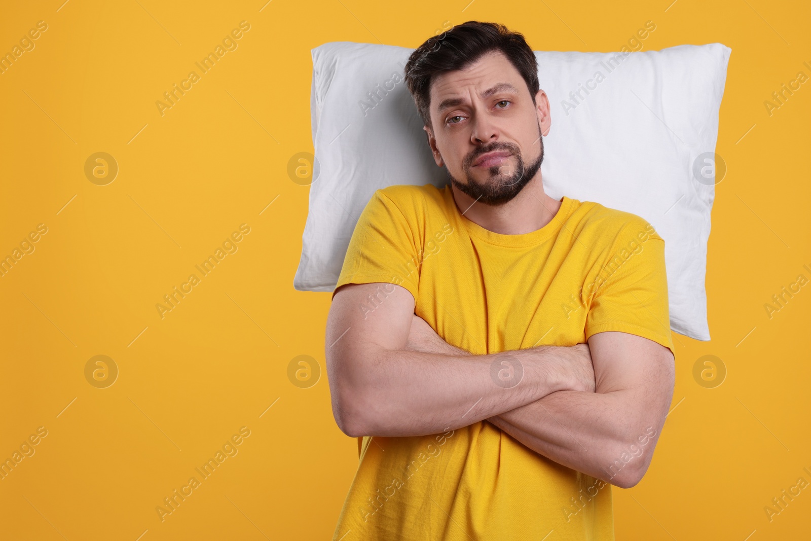 Photo of Tired man with pillow on yellow background, space for text. Insomnia problem