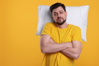 Photo of Tired man with pillow on yellow background, space for text. Insomnia problem