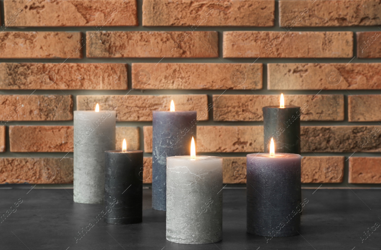 Photo of Burning candles on table against brick wall