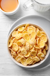 Tasty crispy corn flakes served with milk and honey on white wooden table, flat lay