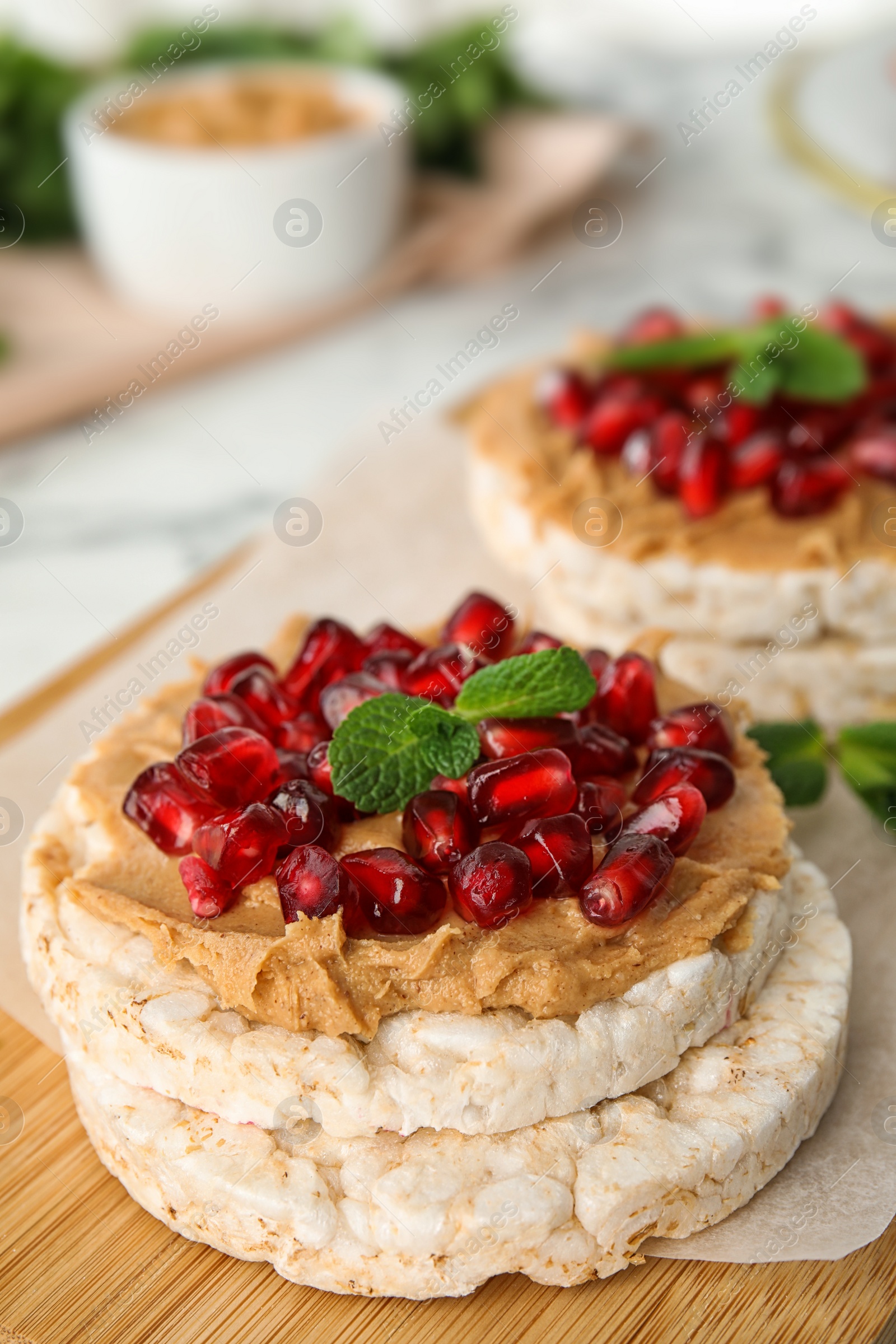 Photo of Puffed rice cakes with peanut butter, pomegranate seeds and mint on wooden board, closeup