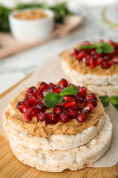 Photo of Puffed rice cakes with peanut butter, pomegranate seeds and mint on wooden board, closeup