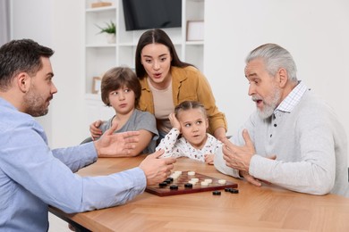Photo of Emotional family playing checkers at table in room