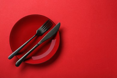 Clean plate with cutlery on red background, top view. Space for text