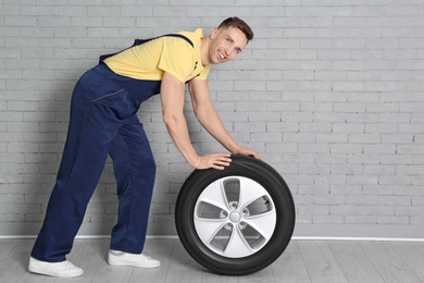 Male mechanic with car tire on brick wall background