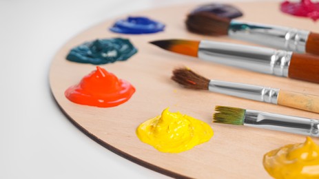 Photo of Artist's palette with samples of colorful paints and brushes on white table, closeup