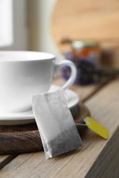 Photo of Tea bag and cup on wooden table indoors, closeup