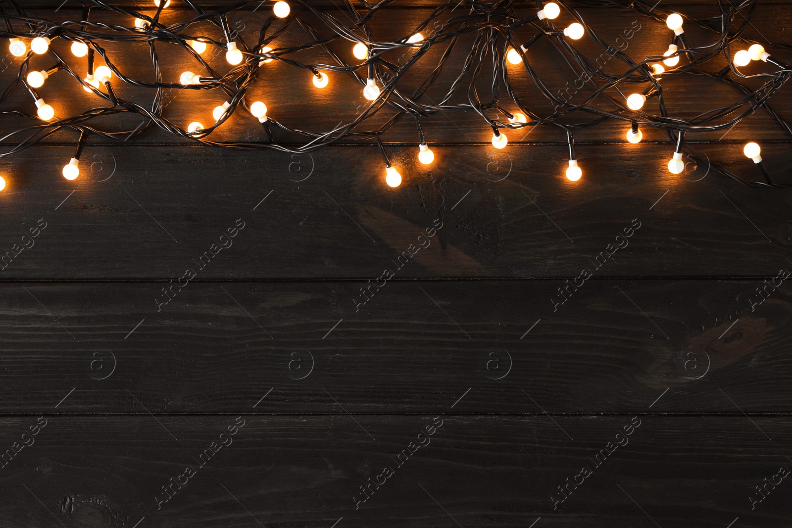 Photo of Glowing Christmas lights on dark wooden background, top view. Space for text