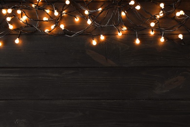 Glowing Christmas lights on dark wooden background, top view. Space for text