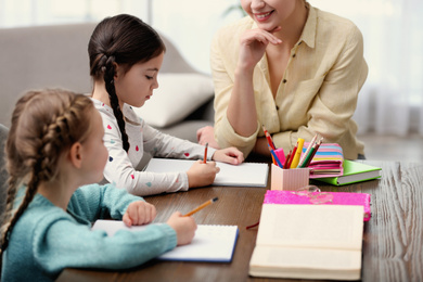 Photo of Little girls doing homework with mother at table indoors