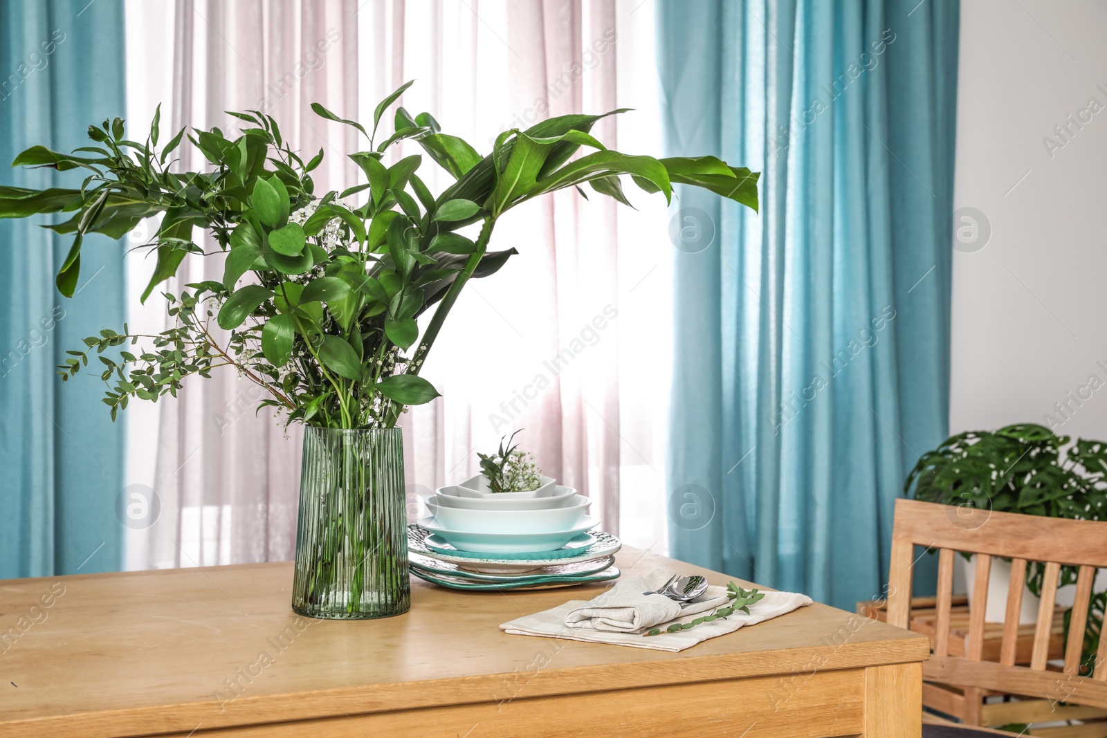 Photo of Dishware and plants on wooden table near window with elegant curtains