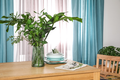 Dishware and plants on wooden table near window with elegant curtains