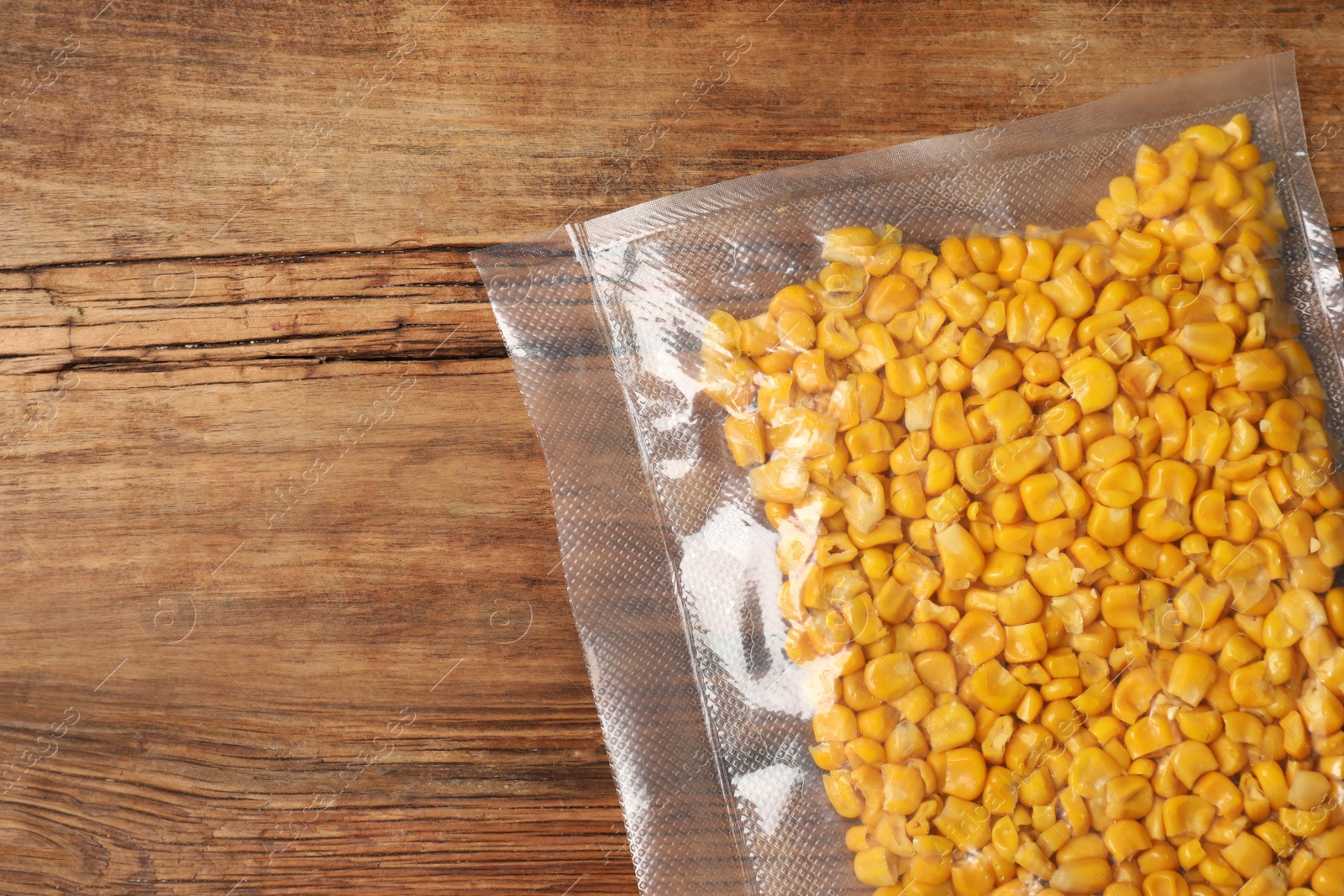 Photo of Vacuum pack of corn on wooden table, top view. Space for text