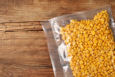 Photo of Vacuum pack of corn on wooden table, top view. Space for text