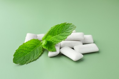 Tasty white chewing gums and mint leaves on light green background, closeup