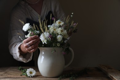 Photo of Woman creating beautiful flower arrangement at wooden table, closeup. Space for text