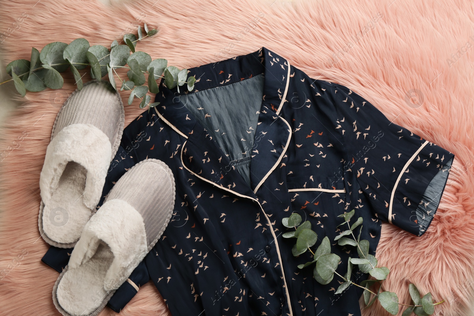 Photo of Pair of fluffy slippers, pajamas and eucalyptus branches on fuzzy carpet, flat lay. Comfortable home outfit